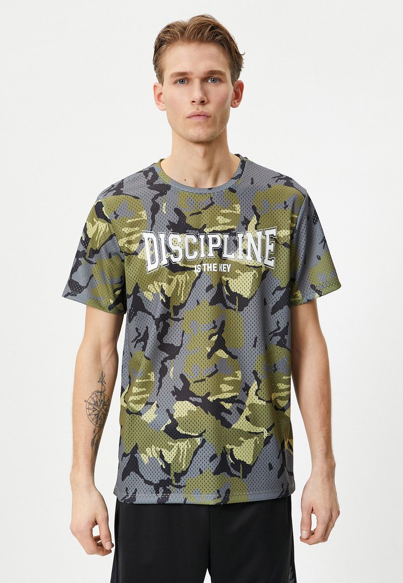 Camiseta de patrón de camuflaje en gris y verde, con un diseño de malla texturizada y el texto "LA DISCIPLINA ES LA CLAVE" en letras blancas.