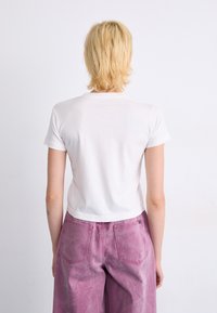 White short-sleeve t-shirt paired with high-waisted, pink denim pants displayed from the back. The fabric appears soft with minimal detail.