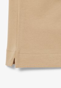 Beige stickad tyg med en texturerad yta; har en sidoklyvning och rena kanter. Materialet verkar lätt och genomträngligt.