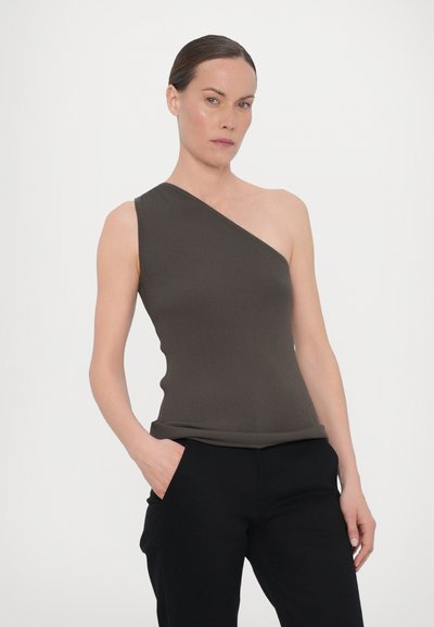 Top de um ombro, canelado, em verde oliva escuro, apresentando um design ajustado e uma textura suave. Combinado com calças pretas, o modelo está de pé com confiança.