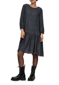 Schwarz-weiß kariertes Kleid mit Dreiviertelärmeln, rundem Ausschnitt und Rüschensaum. Getragen mit schwarzen Knöchelstiefeln.