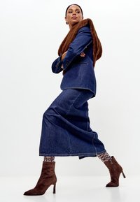 Donkerblauwe denim colbert en rok, gecombineerd met een bruine bonten sjaal. Bruine suède enkellaarsjes en gestreepte panty's maken de look compleet.