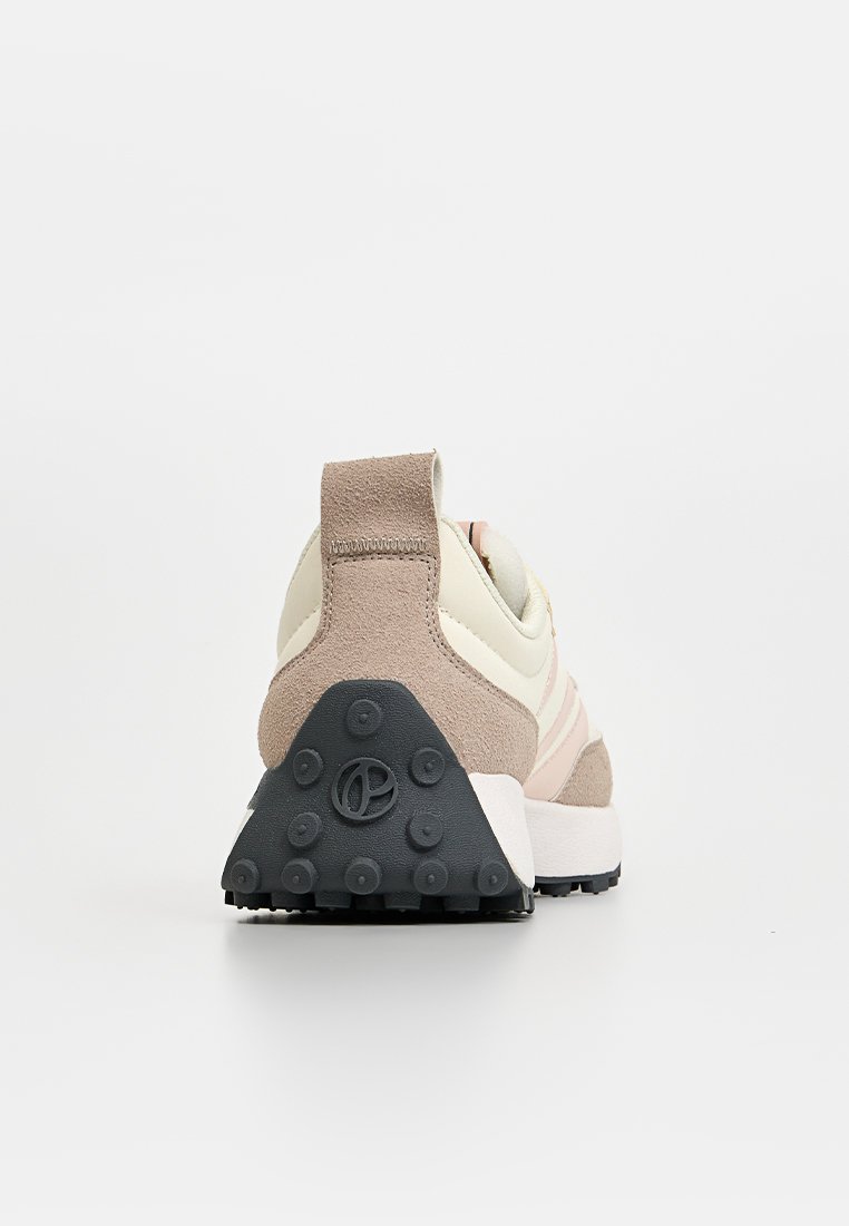 Zapatilla con parte superior en beige y amarillo pálido, parte trasera de gamuza, franjas rosas y suela de goma negra texturizada con agarres circulares.