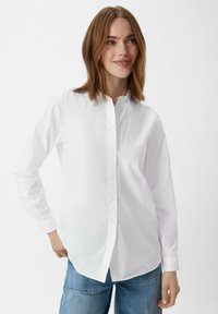 Witte button-up shirt met een klassieke kraag, lange mouwen, een gladde textuur en zijsplitten, gecombineerd met blauwe jeans.