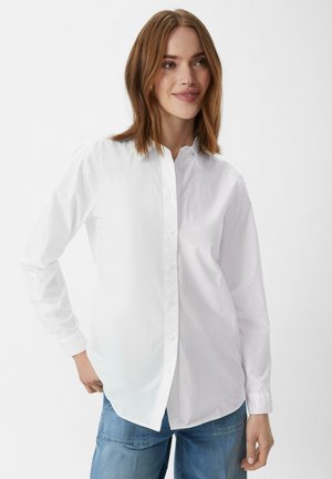 White button-up shirt with a classic collar, long sleeves, smooth texture, and side slits, paired with blue jeans.