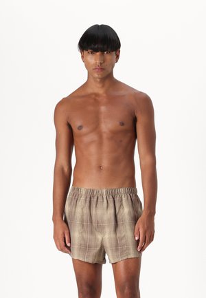 Short de bain à carreaux marron et beige avec une taille élastique, en matériau léger et à coupe décontractée, porté par un mannequin torse nu sur fond blanc.