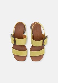 Gule tekstil sandaler med to brede remmer, brun lærsåle og en skjellmønstrete spenne. Lav strukturert hæl.