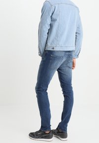 Vaaleansininen farkkutakki, jossa on hieman lyhyt leikkaus, yhdistettynä tummansinisiin kapeisiin farkkuihin ja mustiin urheilujalkineisiin.