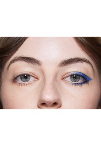 Närbild av ett ansikte med blå eyeliner på ena ögat, som kontrasterar med naturlig makeup på det andra. Huden är ljus med en lätt textur.