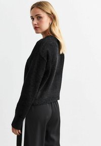 Maglione cropped nero e peloso con scollatura rotonda e maniche lunghe, abbinato a pantaloni neri con una striscia laterale bianca.