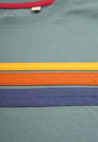 Kurzarmhemd aus grüner Baumwollstruktur mit horizontalen Streifen in Gelb, Orange und Marineblau sowie einem kastanienbraunen Rundhals.