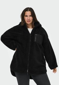 Melna polāra jaka ar kapuci, pārāk liels izmērs, teksturēta virsma, pilns zippers un neliela kabata ar zippers uz krūts. Mīksts un silts materiāls.