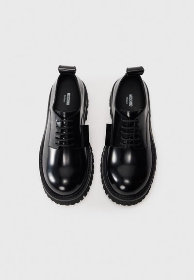 Black leather shoes with a shiny finish, round toe, lace-up design, and chunky treaded sole. Features a pull tab at the back.