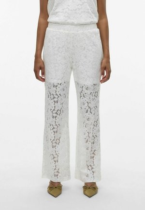 Weiße Spitzenhose mit Blumendessin, weit geschnittenen Beinen, elastischem Bund und durchscheinenden unteren Abschnitten, kombiniert mit spitzen Schuhen.