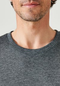 Camiseta de cuello redondo gris oscuro con una textura suave, con un cuello ligeramente acanalado y detalles de costura visibles.