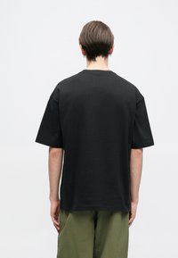 Black short-sleeve T-shirt with a relaxed fit and a crew neckline. Made from soft cotton, features minimal stitching and a smooth texture.