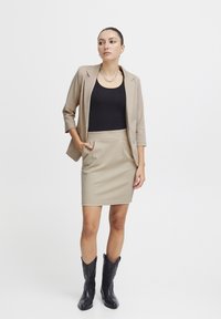 Blazer beige, débardeur noir et jupe crayon beige. Porte des bottes de cow-boy noires. Présente une texture lisse et un design structuré.