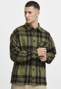Groen en zwart geruit flanellen overhemd, met een knoopsluiting aan de voorkant, kraag en een enkel borstzakje met een flap. Zachte textuur.