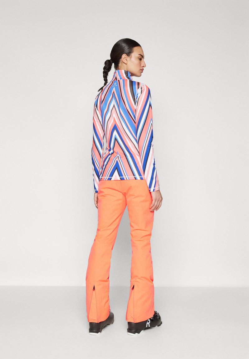 Langärmliges Fleece-Oberteil mit einem mehrfarbigen Zickzackmuster; kombiniert mit hochgeschnittenen, leuchtend orangefarbenen Hosen mit Reißverschluss am Saum.