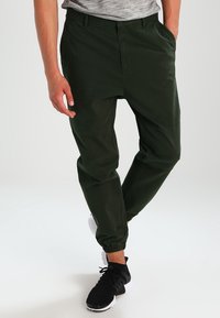 Ciemnozielone spodnie dresowe wykonane z lekkiego materiału, z elastycznymi mankietami, kieszeniami bocznymi i luźnym krojem.