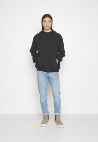Zwarte hoodie met een voorste kangoeroezak, gecombineerd met lichtblauwe jeans en grijze hoge sneakers. Eenvoudig, casual ontwerp.