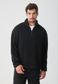 Pullover in pile nero con zip a un quarto, tessuto texturizzato, vestibilità comoda e maniche lunghe. Il colletto di mezzo pollice offre una copertura aggiuntiva.