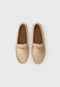 Mocassins en daim beige avec bout rond, détails de couture, lacet central et semelle intérieure lisse couleur tan. Nom de la marque "BOSS" embossé à l'intérieur.