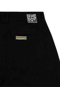 Pantalon noir avec deux étiquettes de la marque "homeboy" : un patch brodé près de la taille, une étiquette en tissu colorée sur la poche arrière.