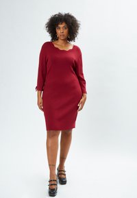 Burgunderfarbenes Strickkleid mit einem gewellten Ausschnitt, Dreiviertelärmeln und einer taillierten Silhouette, das Bindebänder an den Ärmelenden hat.