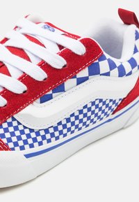 Sneaker in tessuto a scacchi rosso e blu con lacci bianchi, colletto imbottito e suola in gomma bianca con dettagli e cuciture blu.