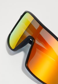 Schwarz gerahmte Sonnenbrille mit großen, verlaufenden Gläsern in Gelb- und Orangetönen, die ein elegantes, rundum laufendes Design betonen.