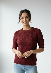 Bordowy sweter z dzianiny z fakturowanym wzorem fal, krótkimi rękawami i okrągłym dekoltem, zestawiony z jasnoniebieskimi dżinsami.