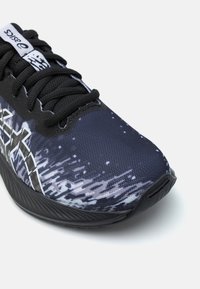 Chaussure de sport noire avec une tige en mesh texturée, présentant un motif abstrait bleu et blanc, un bout rond et une semelle noire rembourrée.