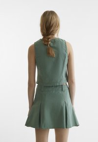 Grønn avkortet topp og matchende skjørt laget av lettvektig stoff. Skjørtet har innlegg og sømdetaljer. Minimalistisk design, bakfra.