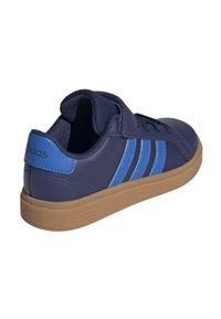 Zapatilla deportiva de color azul oscuro con acentos azules, parte superior texturizada, tira de velcro y suela de goma color marrón claro. Presenta tres franjas azules en el lateral.