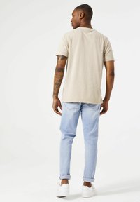 Camiseta de manga corta en beige claro con escote redondo, combinada con jeans de mezclilla azul claro, puños doblados y zapatillas blancas.