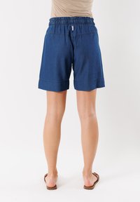 Pantalones cortos de mezclilla con cintura elástica, color azul medio, dobladillo vuelto y un ajuste relajado. La tela parece ligera con costuras visibles.