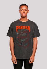 Schwarzes übergroßes T-Shirt mit einem Grafikdesign eines Schlangens und "PANTERA" in fetten orangefarbenen Buchstaben. Aus Baumwollmaterial mit einem abgenutzten Look.