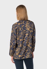 Floral-patterned top in brown and navy, featuring a relaxed fit, long sleeves, and a crew neckline. Smooth fabric with a soft texture.