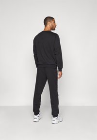 Svart genser og matchende bukser, begge med en avslappet passform. Buksene har hvite sidestriper. Fottøy: hvite joggesko med detaljer.