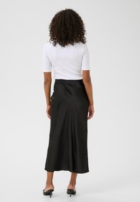 Jupe midi en satin noir avec une texture lisse, qui tombe élégamment et présente un léger éclat. Associée à un haut blanc ajusté.