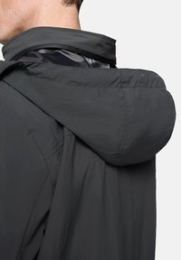 Ciemnoszara, lekka kurtka z kapturem, o gładkiej fakturze i widocznych szwach. Kołnierz jest lekko podniesiony i miękki.