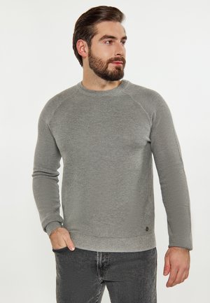 Grå strikket sweater med en struktureret overflade, rund halsudskæring og raglanlange ærmer. Har en diskret logoaccent ved kanten.