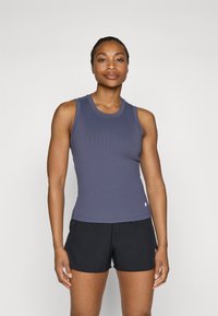 Marineblå ribbestrikket tanktop med rund hals og slank passform, paret med svarte shorts. Har subtil logo-detaljering. Jevn tekstur.