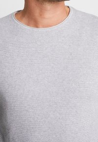 Ljust grått stickat tröja med rund halsringning, med ett texturerat zigzagmönster och en mjuk, slät finish.