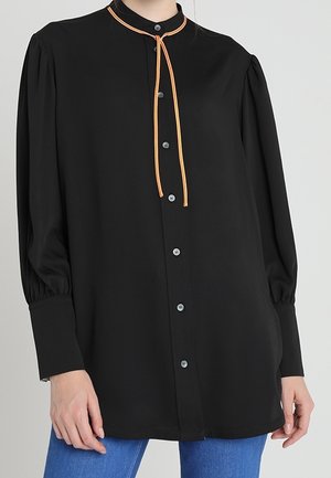Black long-sleeve blouse with puffed shoulders, button-down front, and thin orange tie detail at the round neckline, worn with blue jeans.