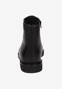 Bottines en cuir noir avec une texture lisse, une forme arrondie et des détails de fermeture éclair à l'arrière. Semelle plate en caoutchouc.