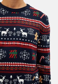 Knitted navy sweater with white reindeer, snowflakes, gingerbread men, and candy canes in festive patterns with red and green accents.