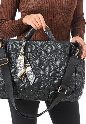 Black quilted bag with floral pattern, featuring shiny fabric, dual handles, and a detachable patterned scarf accent. Adjustable shoulder strap.