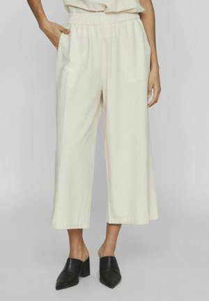 Helle, cremefarbene Weitbein-Hosen mit einem elastischen Bund, die seitliche Taschen und eine weiche Stofftextur aufweisen. Kombiniert mit schwarzen Mules.